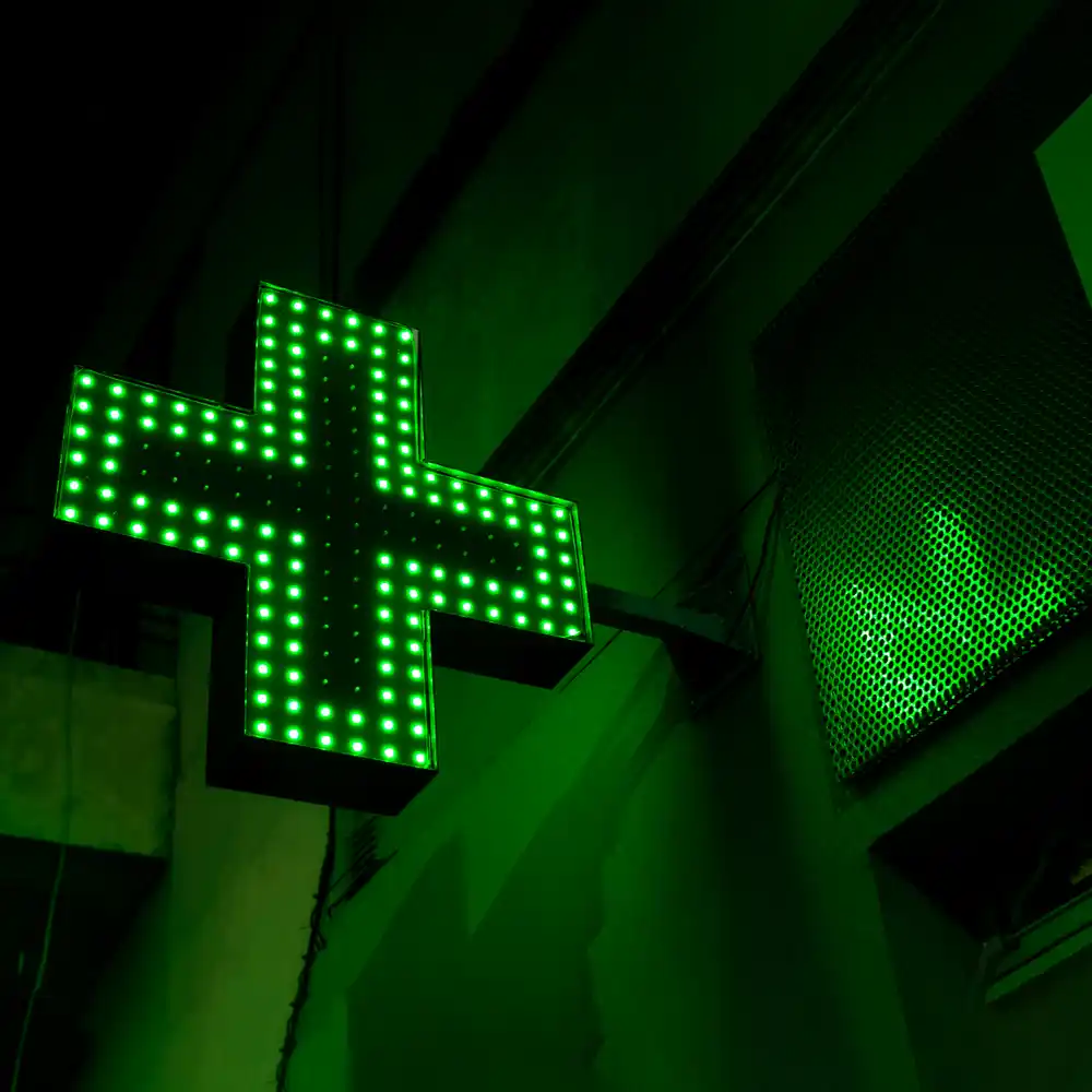 La croce verde luminosa di una farmacia, accesa di notte sopra la strada