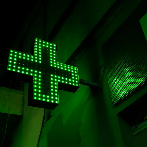 La croce verde luminosa di una farmacia, accesa di notte sopra la strada