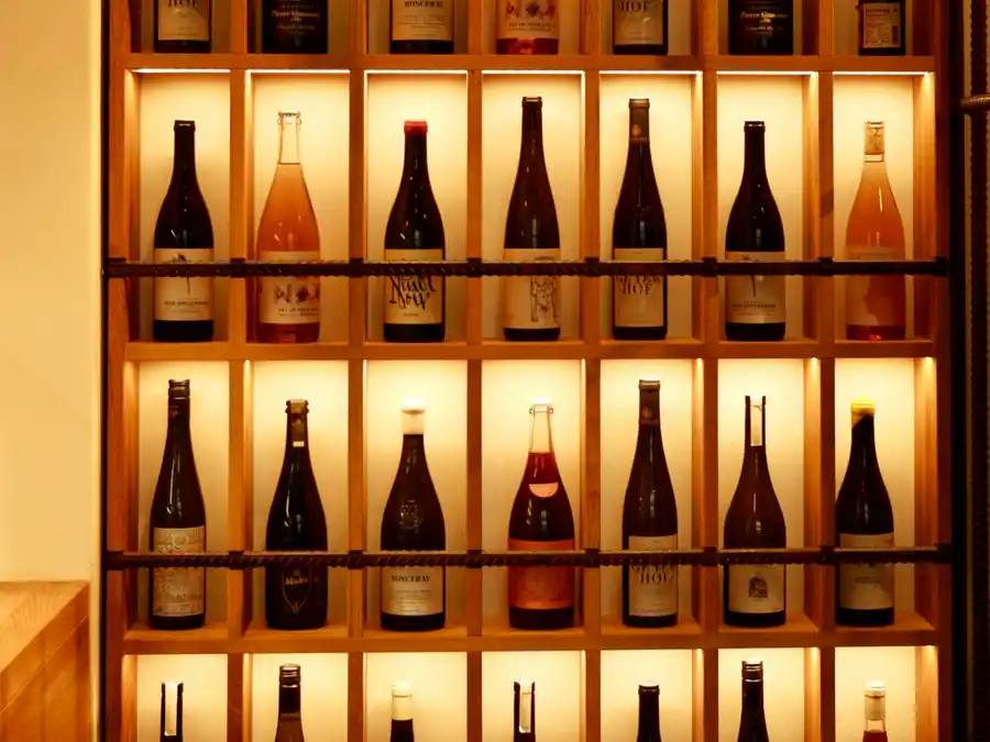 Bottiglie di vino appoggiate su una mensola di legno, nella luce calda della cantina