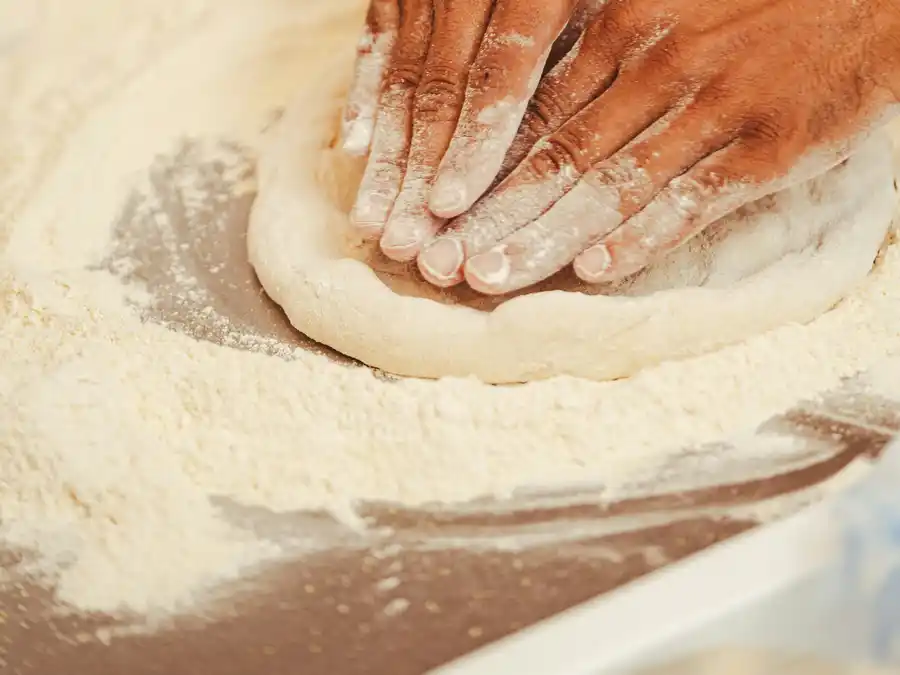 Mani che stendono a mano l'impasto della pizza sulla farina
